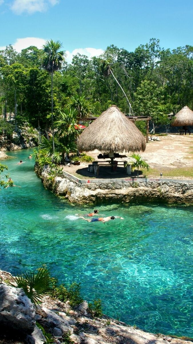 Cénote à ciel ouvert avec eau turquoise cristalline et palapas au toit de palme dans la jungle du Yucatán
