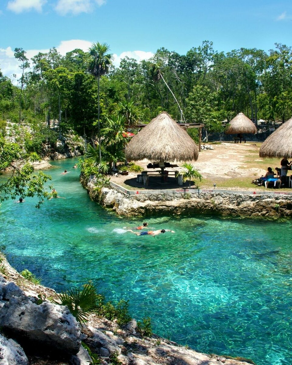 Cénote à ciel ouvert avec eau turquoise cristalline et palapas au toit de palme dans la jungle du Yucatán