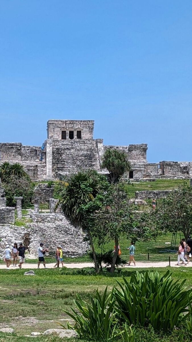 Site archéologique maya de Tulum avec visiteurs explorant les ruines sous un ciel bleu