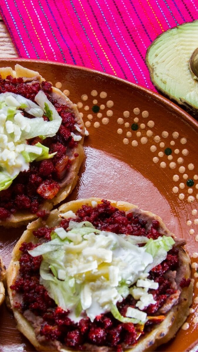 Sopes mexicains garnis de haricots, laitue et fromage servis sur une assiette en terre cuite avec avocat et piment