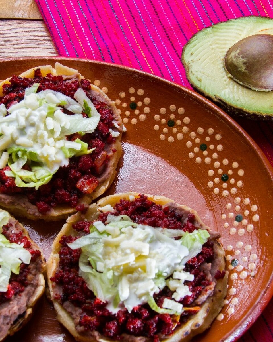 Sopes mexicains garnis de haricots, laitue et fromage servis sur une assiette en terre cuite avec avocat et piment