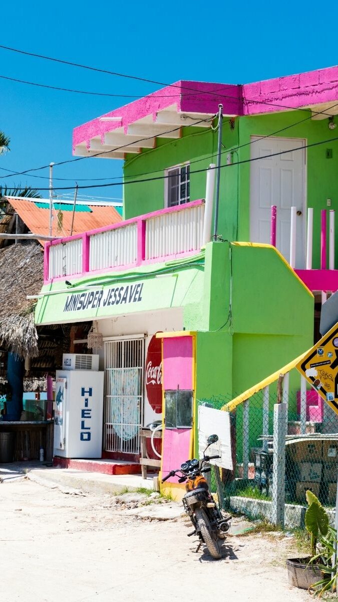 Rue colorée de l'île de Holbox avec maisons roses et vertes, palmiers et palapas