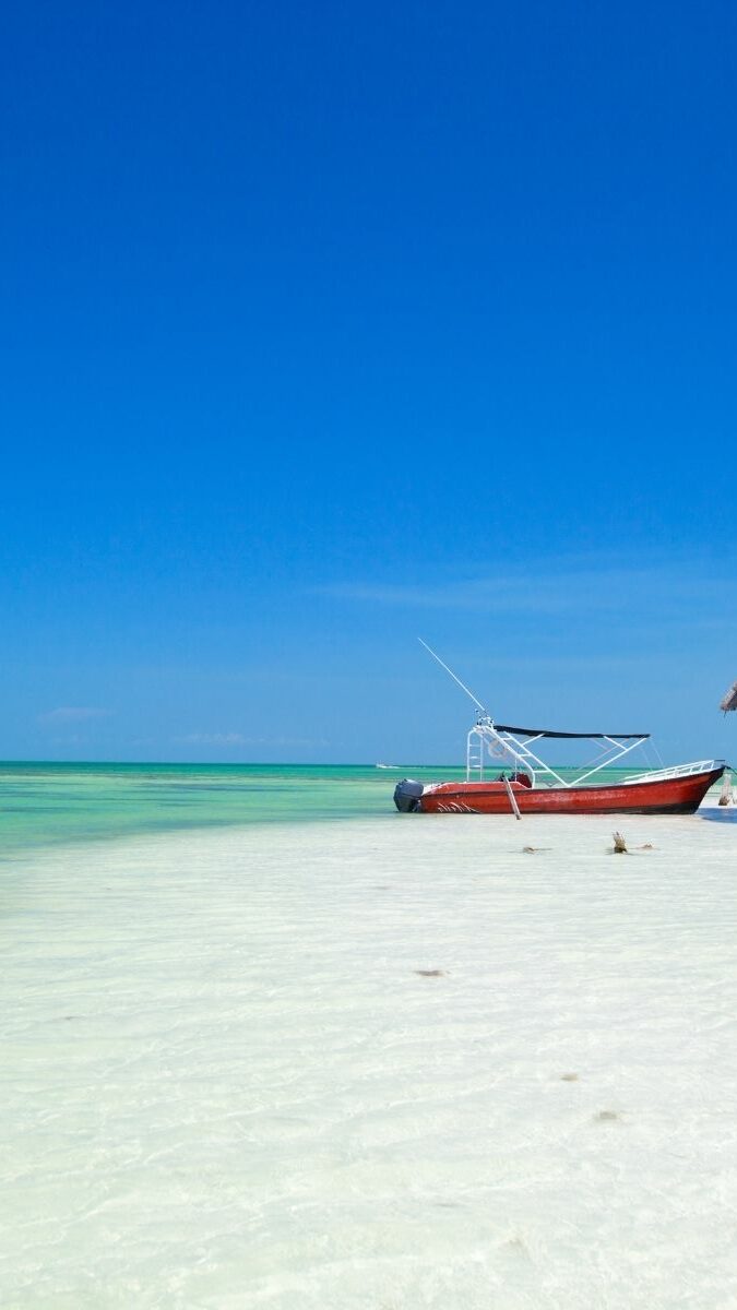Plage de sable blanc de l'île de Holbox avec tour d'observation en bois et bateau rouge