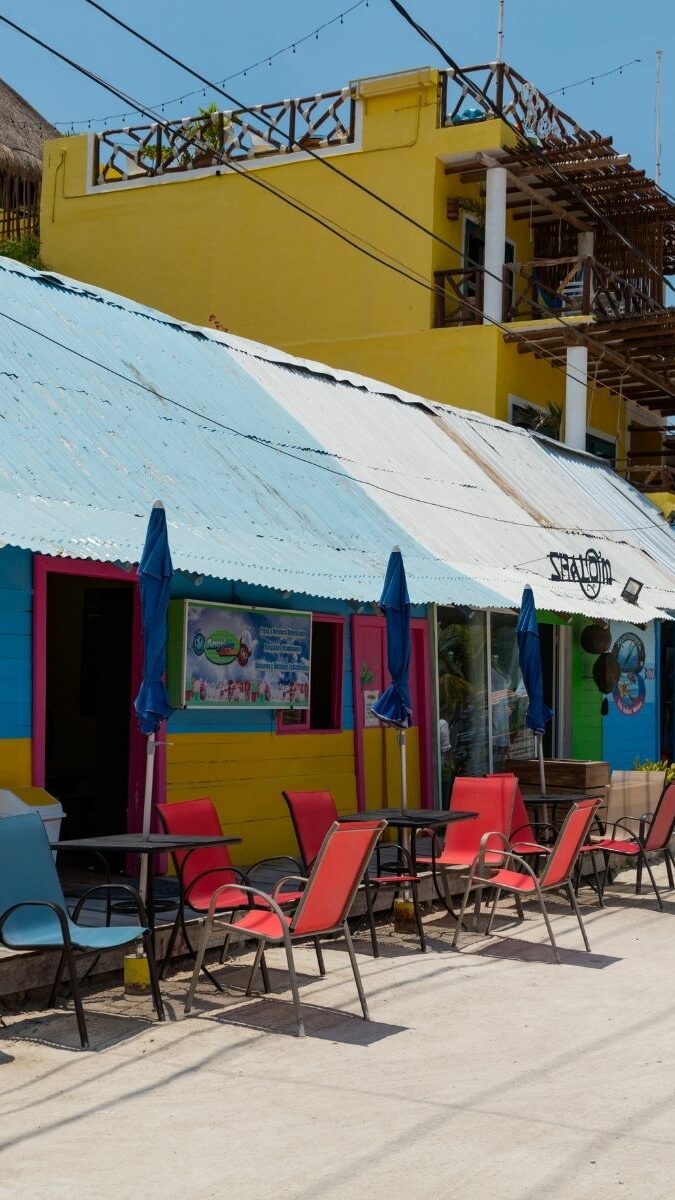 Maisons colorées bleues et jaunes avec chaises sur le trottoir dans le village de Holbox