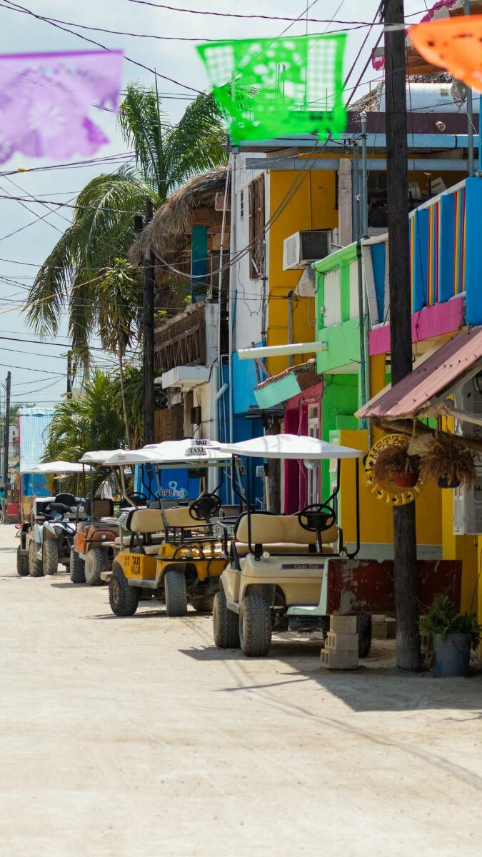 Rue de sable de l'île de Holbox avec voiturettes de golf, maisons colorées et papel picado