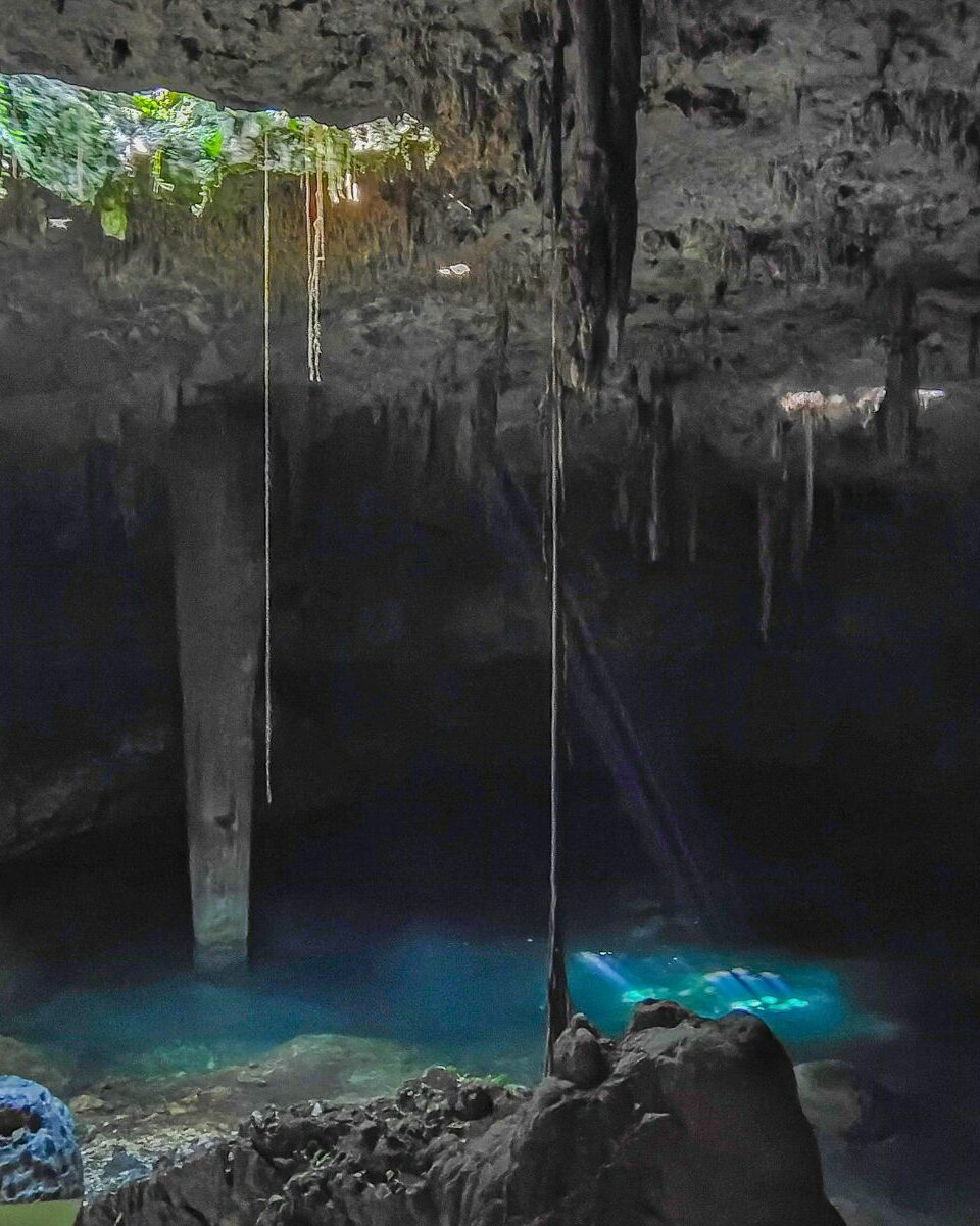 Cénote souterrain avec stalactites, eau bleu profond et ouverture vers la végétation tropicale
