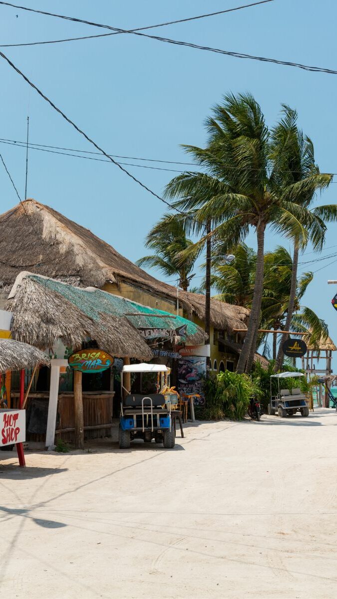 Rue tranquille de Holbox avec palapas au toit de palme, palmiers et maisons colorées