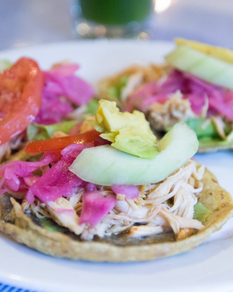 Salbutes yucatèques garnis de poulet effiloché, oignons roses, avocat et tomate