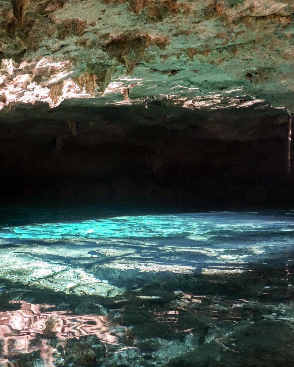 Cénote souterrain aux eaux turquoise illuminées par la lumière naturelle filtrant à travers la roche