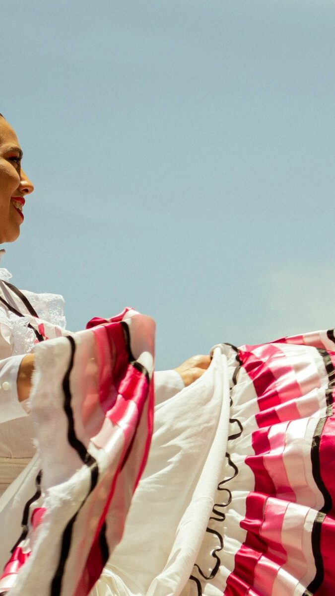 Danseuse folklorique mexicaine en robe blanche et rose virevoltant sous un ciel bleu