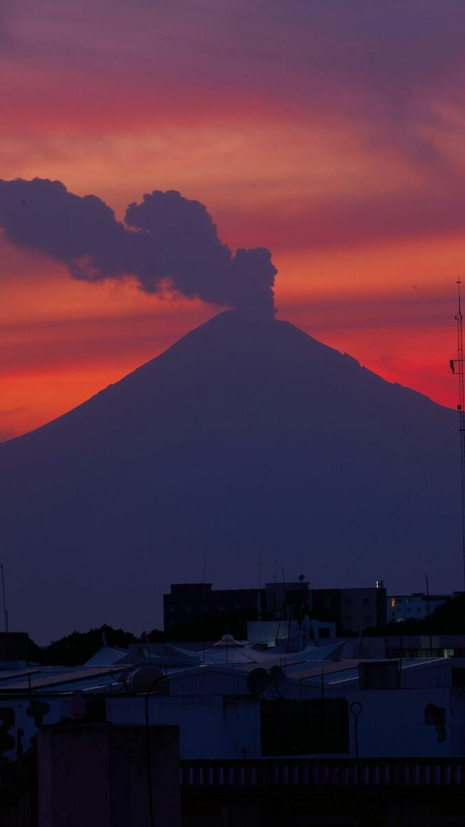 Silhouette du Popocatépetl fumant au coucher du soleil avec ciel rouge et violet sur Puebla